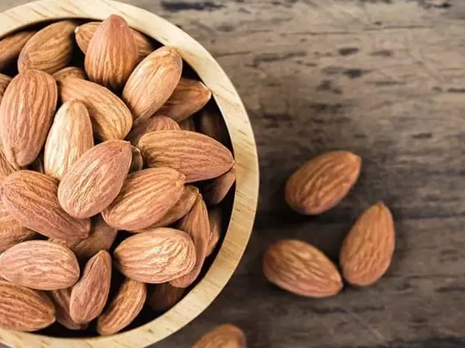 مكسرات لوز: حبات لوز بقشرها البني في طبق خشب، من أنواع المكسرات